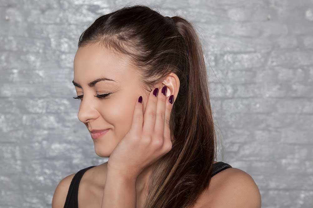 Young woman gently touching her ear as it feels full and clogged, a concern Gomer Hearing Center evaluates in Richardson and Allen, TX